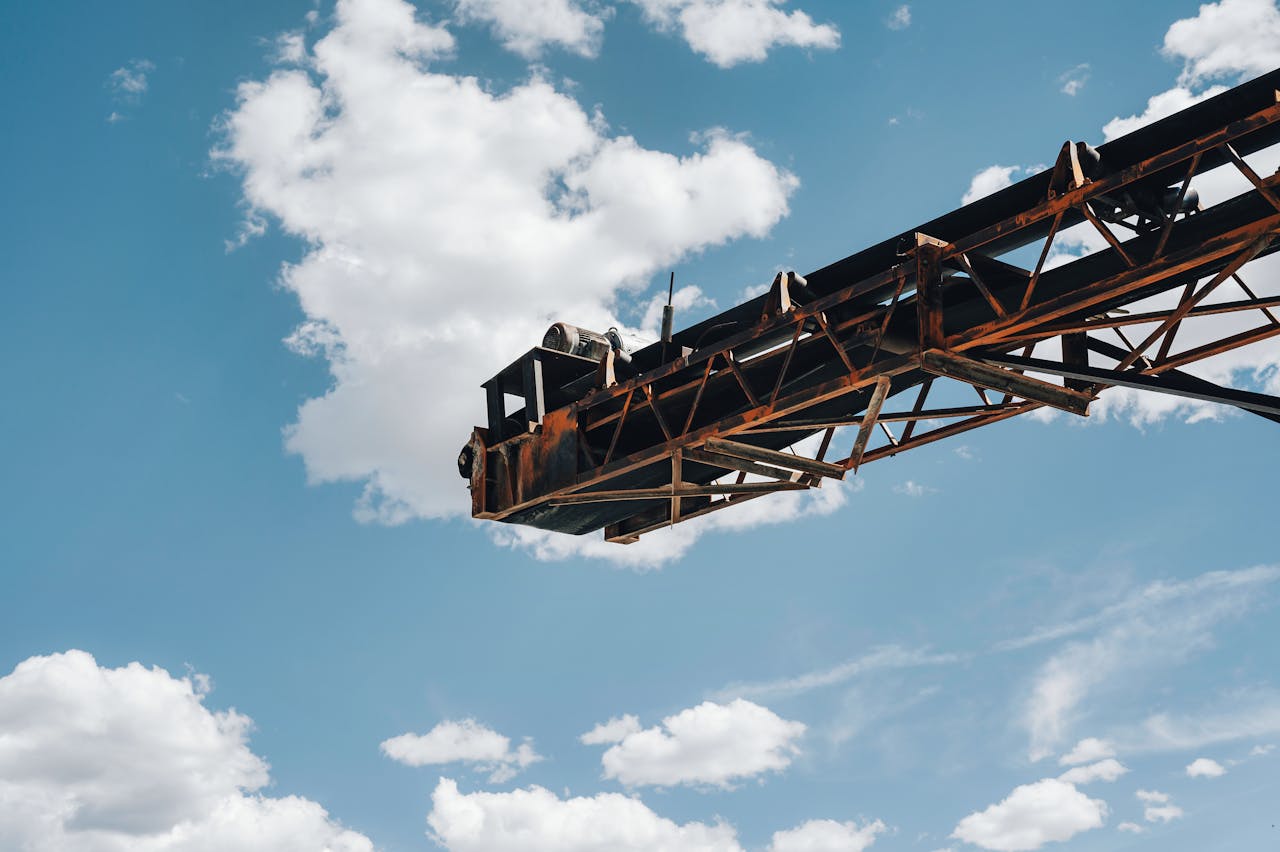 Close-up view of a rusty industrial crane framed against a clear blue sky with scattered clouds.