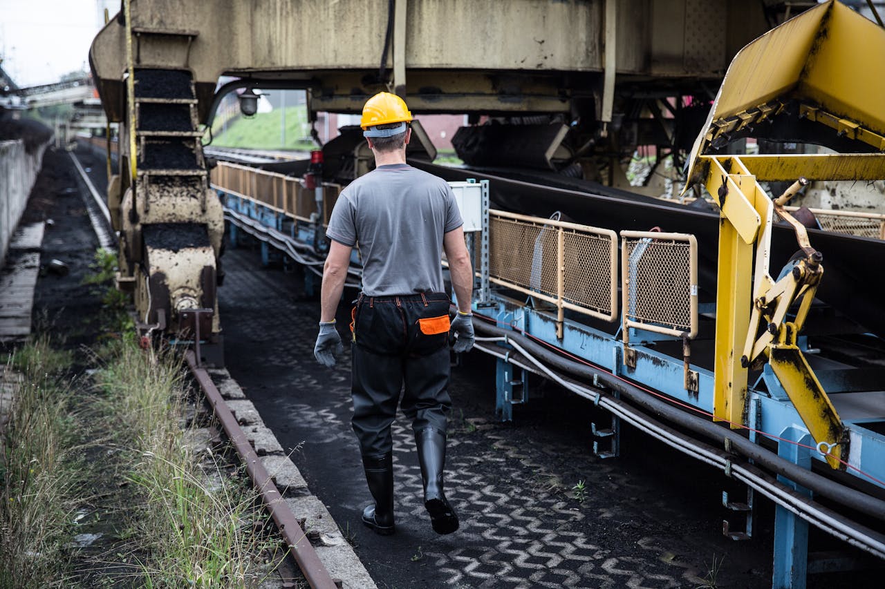 A worker in safety gear examines industrial machinery in an outdoor setting, showcasing industry work.