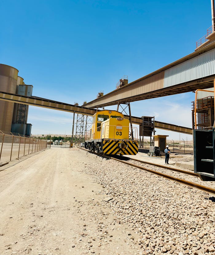 A yellow industrial train at a cement factory track in Saudi Arabia under a clear blue sky.