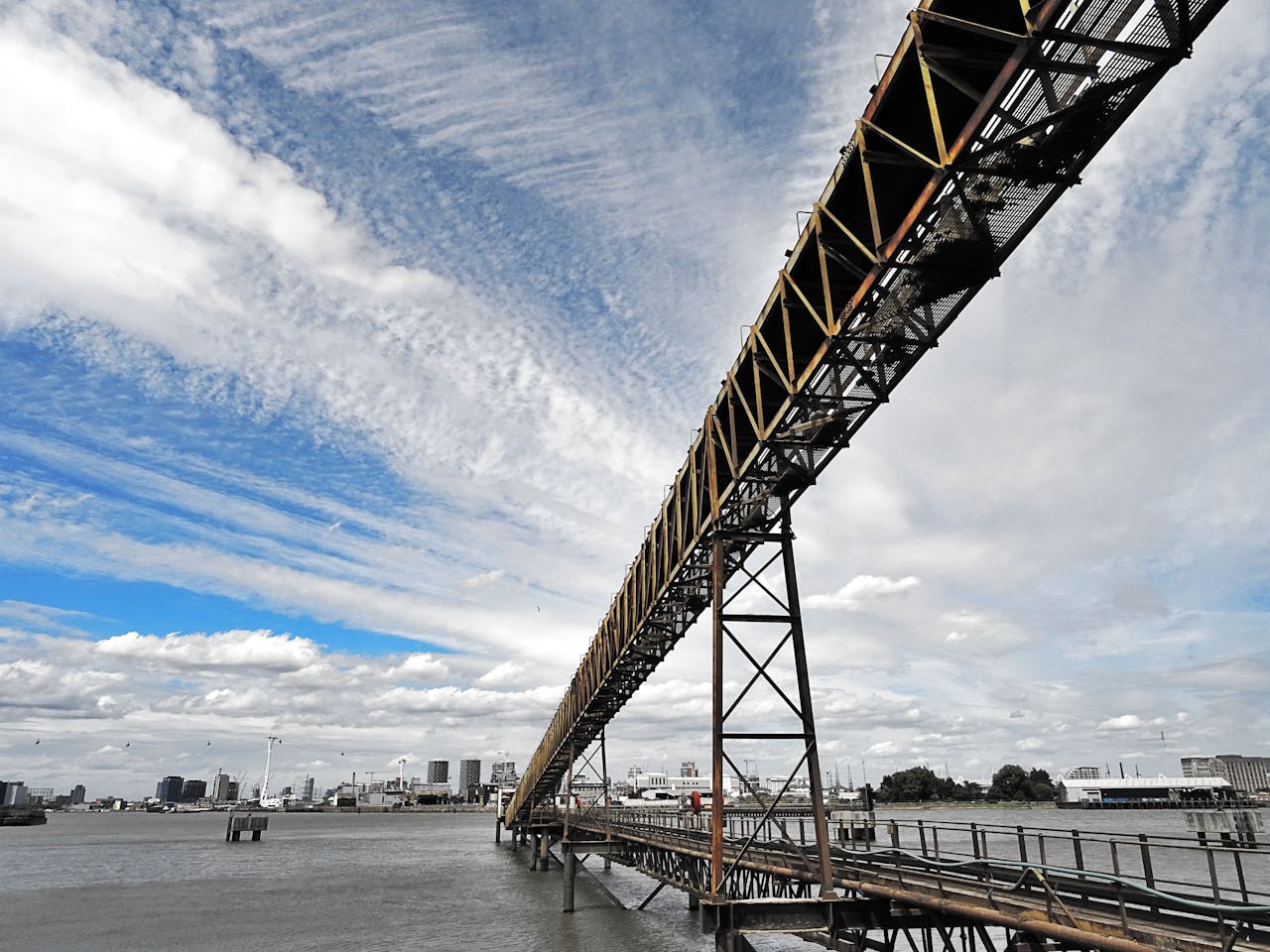 A modern steel bridge stretches over a river with a cityscape in the background. Vivid skyline view.
